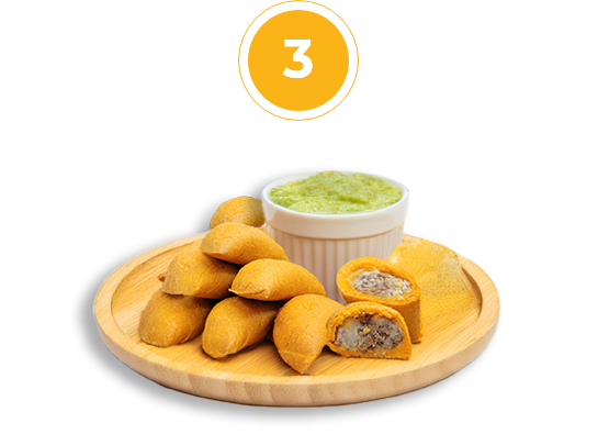 empanadas and cilantro sauce placed on a round wooden cutting board